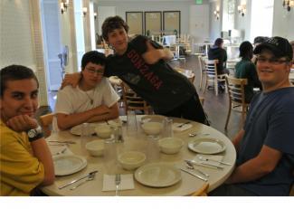 Several smiling YES-2 participants gather around a table in the YES residence in Seattle. The table is set for dinner.